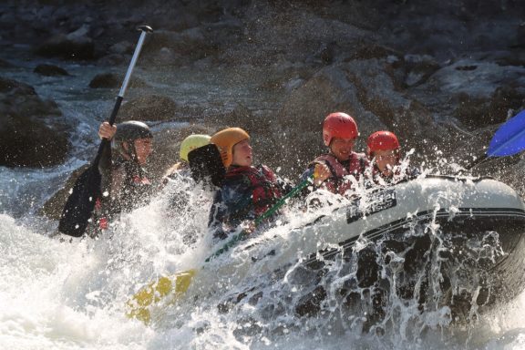 Groupe de personnes en rafting sur une rivière, éclaboussures d'eau autour d'eux.